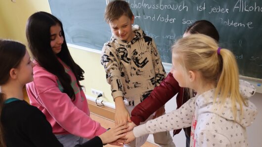 Im Kreis stehende Gruppe von Schülerinnen und Schülern legt die Hände in der Mitte zusammen